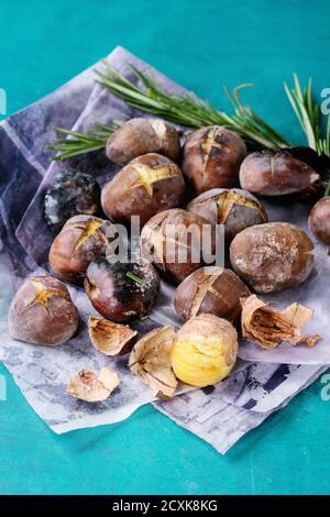 Roasted chestnuts in the ashes with rosemary on paper over bright turquoise wooden background. Close up. Stock Photo