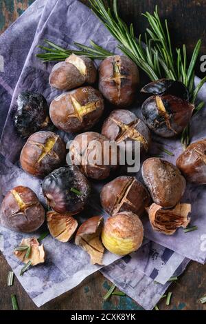 Roasted chestnuts in the ashes with rosemary on paper over old dark texture wooden background. Close up. Stock Photo