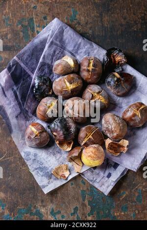 Roasted chestnuts in the ashes on paper over old dark texture wooden background. Top view with space for text. Stock Photo