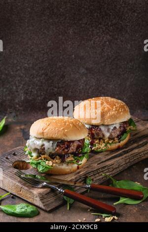 Two hamburgers with beef burger cutlet, fried onion, spinach, ketchup sauce and blue cheese in traditional buns, served on wood chopping board with kn Stock Photo