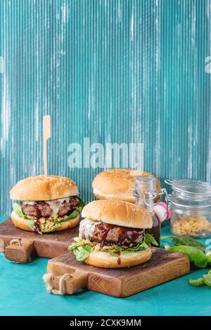 Two hamburgers with beef burger cutlet, fried onion, spinach, ketchup sauce and blue cheese in traditional buns, served on wood chopping board over br Stock Photo