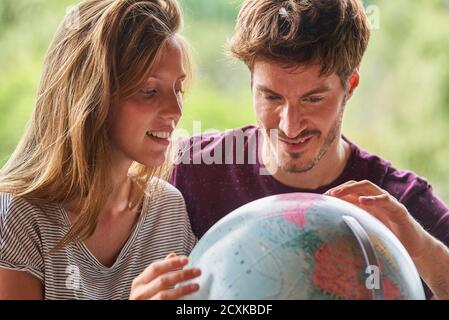 Young couple exploring world globe while sitting in living room Stock Photo