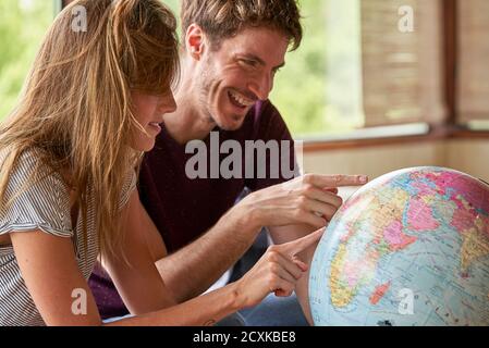 Young couple exploring world globe while sitting on sofa Stock Photo