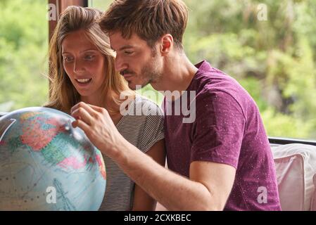 Young couple exploring world globe while sitting on sofa Stock Photo