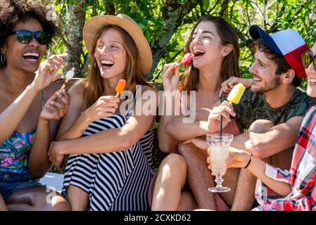 Young friends enjoying drink and ice lolly at poolside Stock Photo
