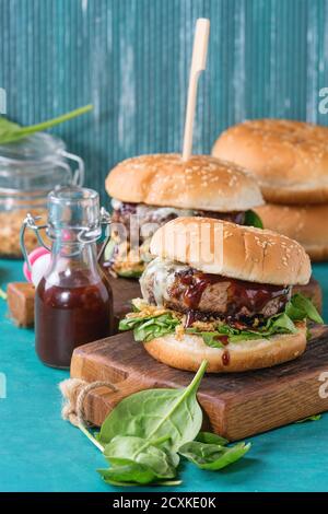 Two hamburgers with beef burger cutlet, fried onion, spinach, ketchup sauce and blue cheese in traditional buns, served on wood chopping board over br Stock Photo