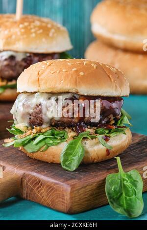 Two hamburgers with beef burger cutlet, fried onion, spinach, ketchup sauce and blue cheese in traditional buns, served on wood chopping board over br Stock Photo