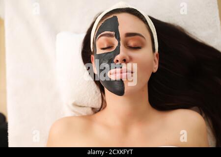 Beautiful woman having clay facial mask apply by beautician. Stock Photo