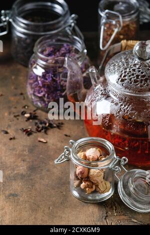 Variety of black, green and herbal dry tea leaves in glass jars with vintage strainer and teapot of hot tea over old dark wooden background. Close up, Stock Photo