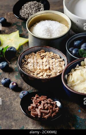 Ingredients for making smoothie for healthy breakfast. Bowls of yogurt, blueberries, granola, almond chia seeds, coconut, milk, chocolate, mint, caram Stock Photo