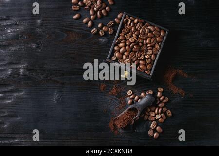 Roasted coffee beans and grind coffee in wood box with scoop over black wooden burnt background. Top view with space. Stock Photo
