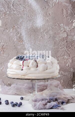 Homemade meringue cake Pavlova with whipped cream, fresh blueberries and blueberry sauce on vintage cake stand on beige concrete texture background, g Stock Photo