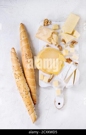 Cheese plate. Assortment of cheese with walnuts and bread on white wood serving board over white concrete texture background. Top view with space. Stock Photo