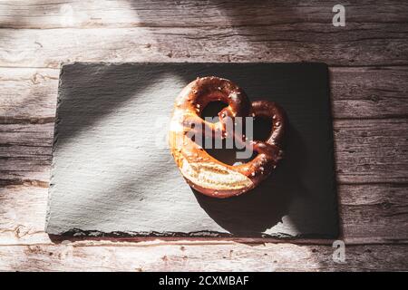 A fresh Pretzel on a slate board rested on a rustic wood table Stock Photo