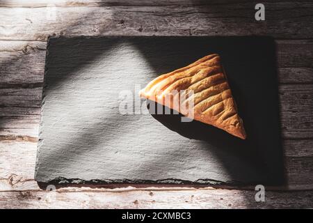 A fresh apple turnover pastry on a slate board resting on a rustic wooden table Stock Photo
