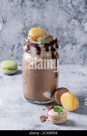 Chocolate coffee milkshake with ice cream scoop served in glass mason jar with retro cocktail tubes and variety of macaroons biscuit on gray texture b Stock Photo