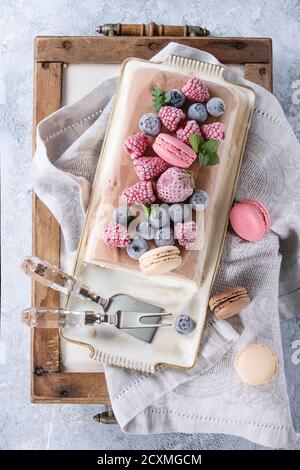 Three layers vanilla, coffee and chocolate ice cream cake, served with frozen berries and macaroons biscuits on rectangular white plate, textile napki Stock Photo