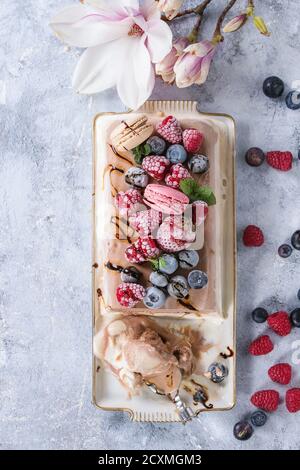Three layers vanilla, coffee and chocolate ice cream cake, served with frozen berries and macaroons biscuits on rectangular white plate, textile napki Stock Photo