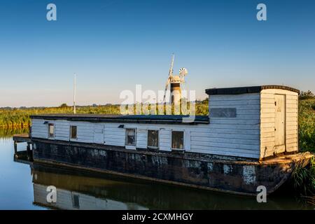 Houseboat on the River Thurne with St Benet's Level Drainage Mill behind.  Norfolk Broads, Norfolk, England. Stock Photo