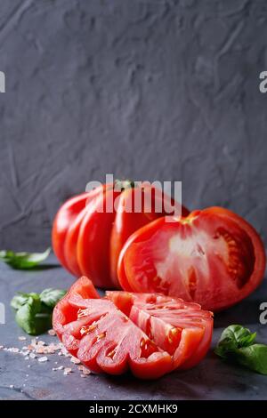 Whole and sliced organic tomatoes Coeur De Boeuf. Beefsteak tomato with pink salt and basil on blue gray metal texture background. Close up with space Stock Photo