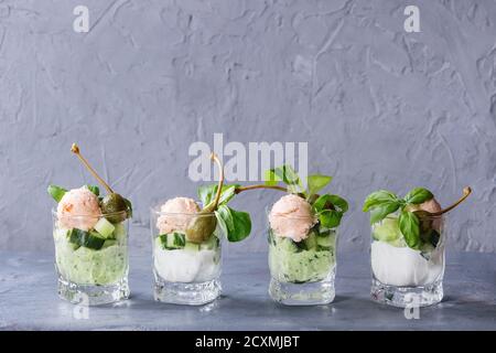Verrines appetizer with salmon pate, red caviar, cucumber, cream cheese, herbs, capers in glasses served over blue gray texture background. Stock Photo