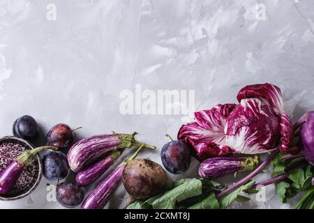 Assortment raw organic of purple vegetables mini eggplants, spring onion, beetroot, radicchio salad, plums, kohlrabi, flower salt over gray concrete b Stock Photo