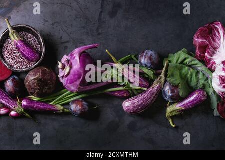 Assortment raw organic of purple vegetables mini eggplants, spring onion, beetroot, radicchio salad, plums, kohlrabi, flower salt over dark metal back Stock Photo