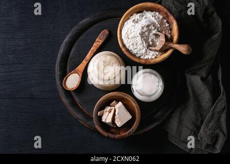 Rye and wheat sourdough in glass jars, fresh and instant yeast, olive wood bowl of flour for baking homemade bread. With spoon, serving board, textile Stock Photo