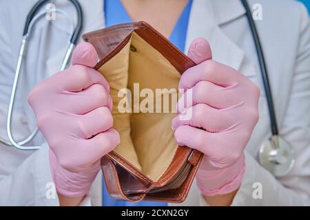 A doctor in medical gloves shows an empty wallet. Nurse in a white coat, the concept of the financial crisis due to coronavirus Stock Photo