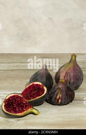 three whole purple figs and one opened on a wooden table with copy space at the background Stock Photo
