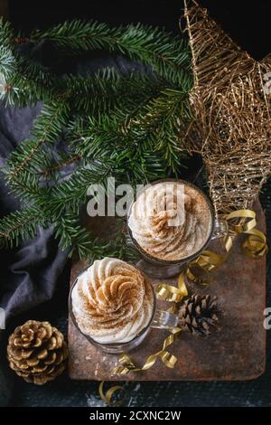 Pumpkin spicy latte  with whipped cream and cinnamon in two glasses standing on clay board with textile and Christmas decoration fir tree other dark b Stock Photo