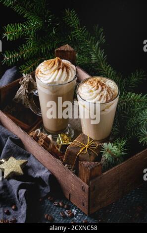 Pumpkin spicy latte  with whipped cream and cinnamon in two glasses standing in wooden board with textile and Christmas decoration and fir tree other Stock Photo