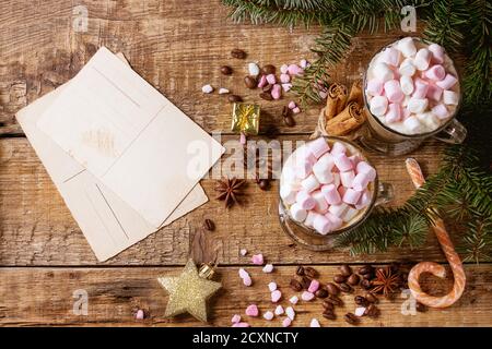 Two glasses of cafe latte with pink marshmallow with empty greeting card, Christmas decor, pink sugar, candy, spices, coffee beans and fir tree over w Stock Photo