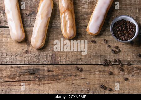 Fresh homemade Coffee eclairs with different glaze and coffee beans over old wooden texture background with space for text. Top view. Stock Photo