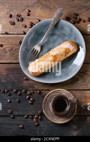 Fresh homemade eclairs with marble glaze on gray plate, coffee beans and ceramic cup of black coffee over old wooden texture background with space for Stock Photo