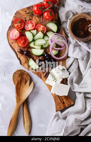 Ingredients for traditional greek salad. Cherry tomatoes, sliced cucumbers, red onion, black olives, feta cheese on olive wood board with loaf bread, Stock Photo