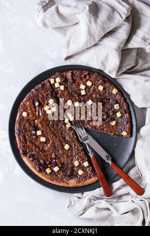 Dessert chocolate pizza with dark, milk, white chocolate, served on black plate with mint and fork over gray concrete background with textile linen. T Stock Photo