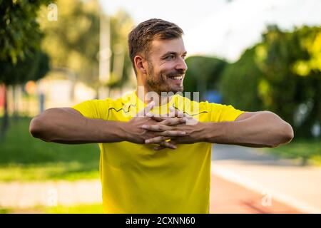 Young man is exercising outdoor. He is stretching his body and warming up for jogging. Stock Photo