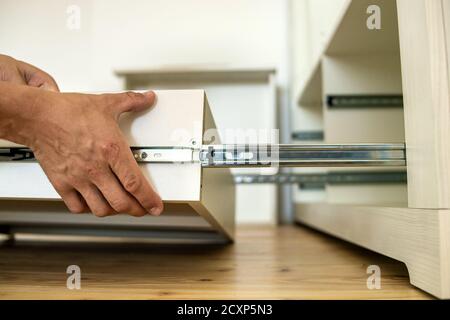 Close up of carpenter hands installing wooden drawer on sliding skids in contemporary cupboard cabinet. Stock Photo