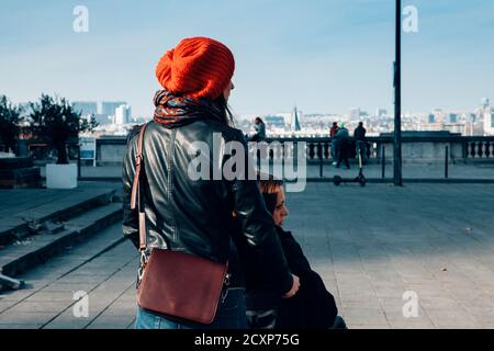 focus on foreground of the back of young woman pushing a wheelchair - an unfocused woman looks elsewhere with a sad look - disabilty handicap concept Stock Photo