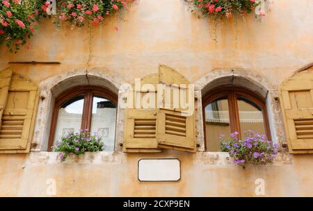 Close-up of the exterior of an urban historic building decorated with beautiful red and purple flowers Stock Photo