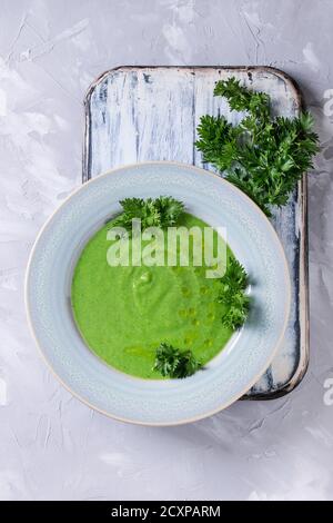 Vegetarian vegan broccoli cream soup served in blue plate with fresh parsley on white serving board over gray concrete background. Top view with copy Stock Photo