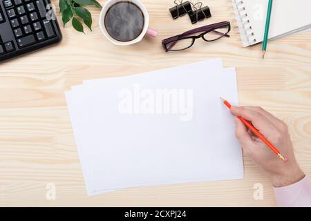 Home office workspace mockup with keyboard, blank paper, notebook and accessories. Man writes on clipboard. Male hands holding a pen and coffee. Flat Stock Photo