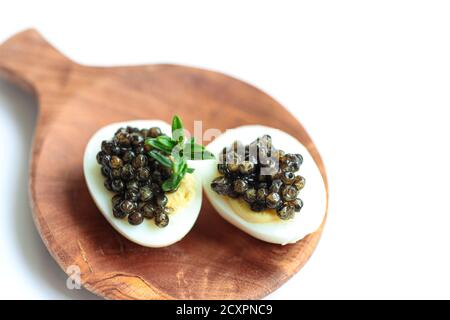 Gourmet dish, delicious black sturgeon caviar on a quail eggs on the wooden plate isolated on the white background Stock Photo