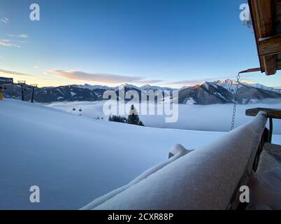 Scenic view to snow covered mountains and a blanket of clouds in the ski resort Saalbach Hinterglemm early in the morning before sunrise Stock Photo
