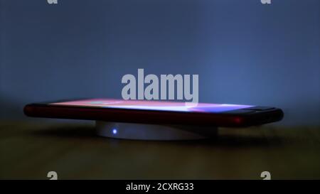 Wireless induction charger base for mobile phone. Moonlight scene while a smartphone is placed on the dock for charging. Stock Photo