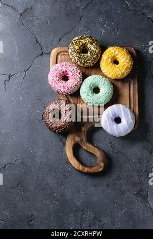 Variety of colorful glazed donuts on wooden serving board over black texture background. Top view with space Stock Photo