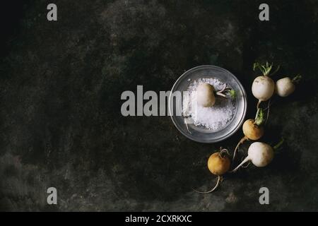 Whole white fresh organic radish in metal plate with sea salt over dark metal texture background. Top view with copy space. Vegetarian concept Stock Photo