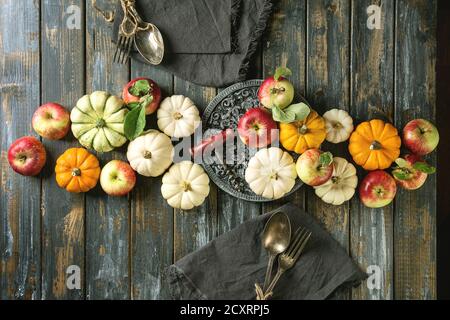 Autumn holiday table decoration setting with decorative pumpkins, apples, red leaves with vintage cutlery, red wine, candle over wooden table. Rustic Stock Photo