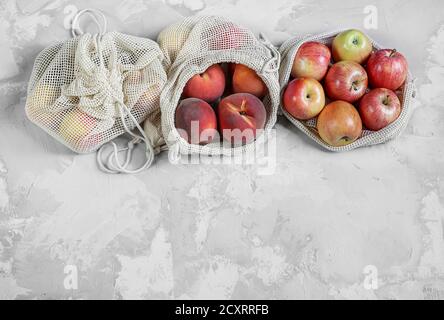Zero waste concept: organic fruits - peaches and apples in reusable eco friendly natural bags on the gray background. Plastic free lifestyle. Stock Photo